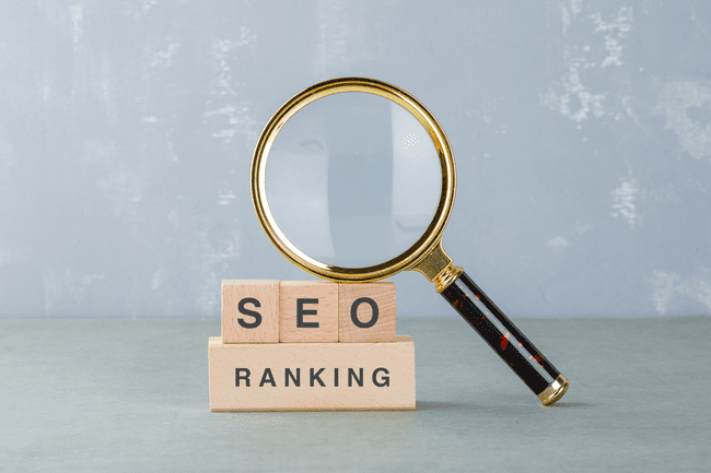 A magnifying glass focused on wooden blocks spelling "SEO" and "RANKING."
