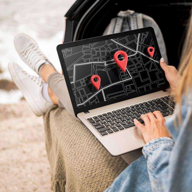 A person sitting outdoors, using a laptop that displays a map with location pins.
