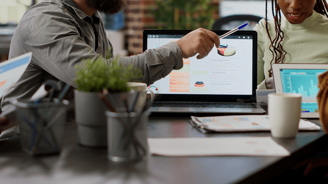 A group of professionals in a meeting, discussing data displayed on a laptop screen with charts and graphs.
