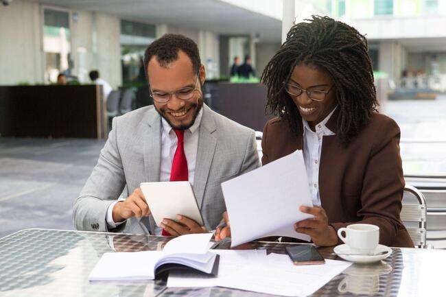 Two business professionals reviewing documents and using a tablet at an outdoor café.