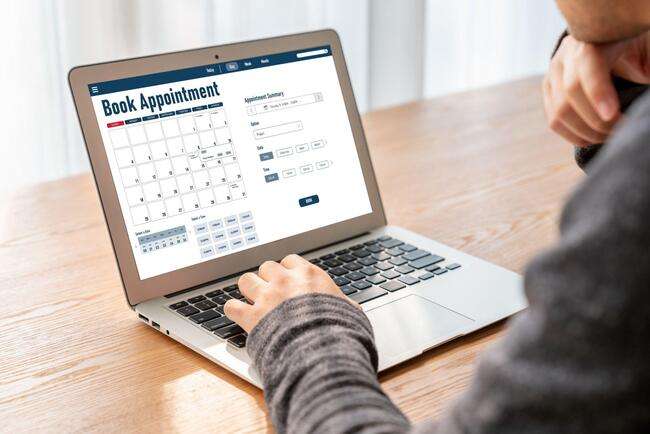 Person using a laptop to book an appointment online, showing a calendar and appointment details on the screen.