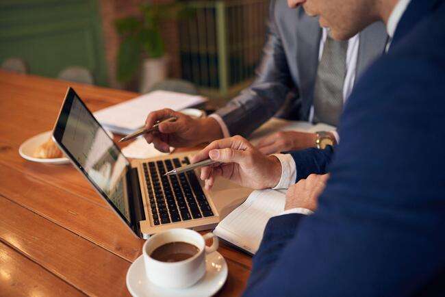 Two business professionals working on a laptop with coffee on the table.