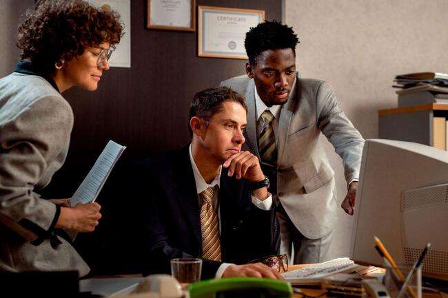 Two men and a lady in suits looking intently at a laptop screen.