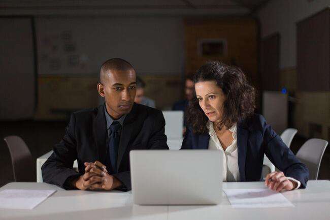 Two legal professionals collaborating on a laptop in an office setting, focusing on document management and case details.