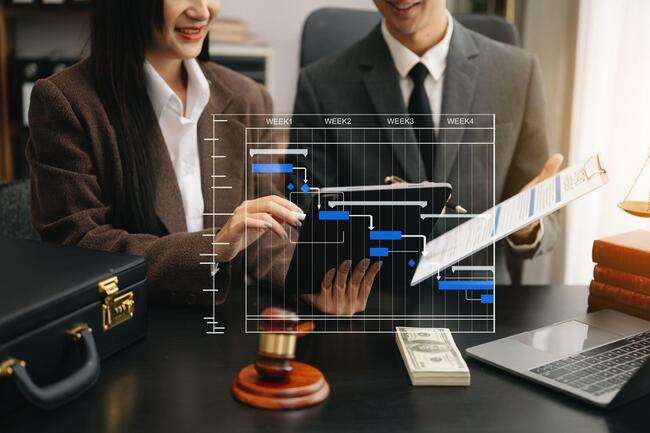 Two legal professionals reviewing a project timeline on a tablet, with legal documents and a gavel in the foreground.