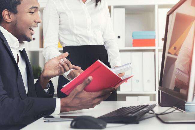 A legal professional discussing a document with a colleague, while working on a computer in an office setting.