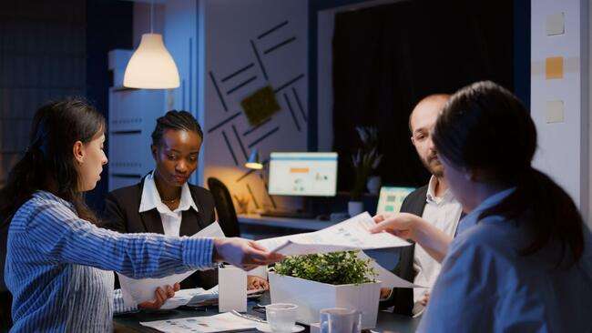 A group of legal professionals working late in the office, collaborating and sharing documents.