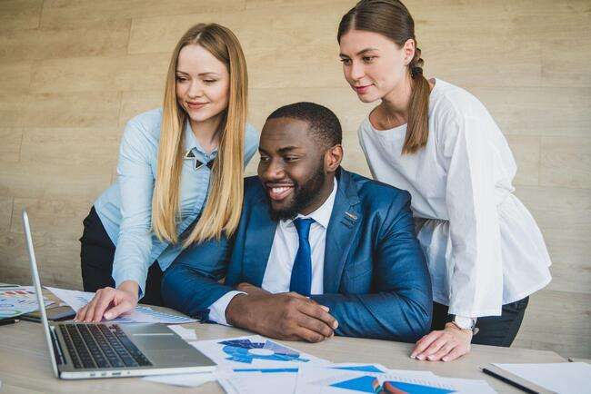 Three legal professionals happily collaborating on a laptop, surrounded by documents and charts.