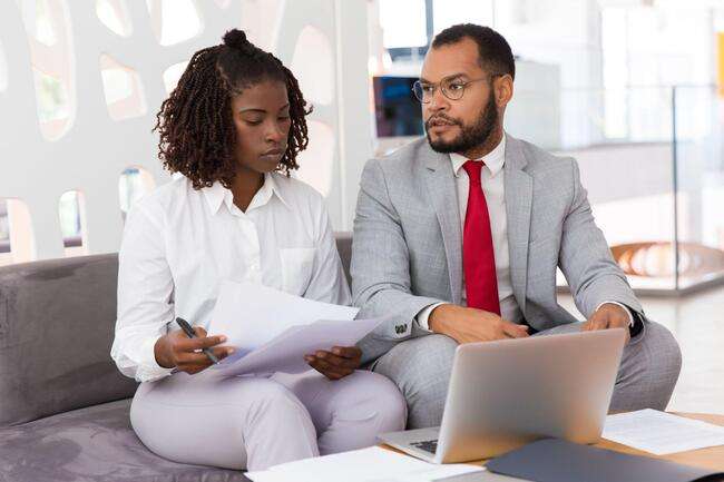 Two legal professionals discussing documents while using a laptop, highlighting teamwork and collaboration.