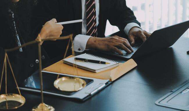 Legal professionals working on a laptop and taking notes, with scales of justice in the foreground.