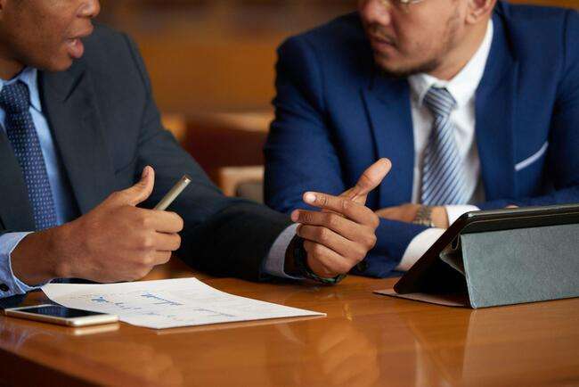 Two legal professionals discussing documents and using a tablet, highlighting detailed collaboration.