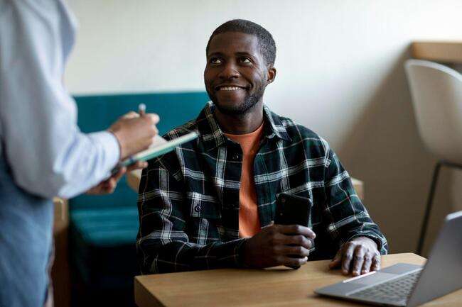 Happy professional holding a phone, engaging in a discussion with a colleague.