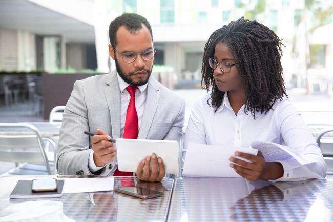 Two professionals reviewing documents together at an outdoor table.