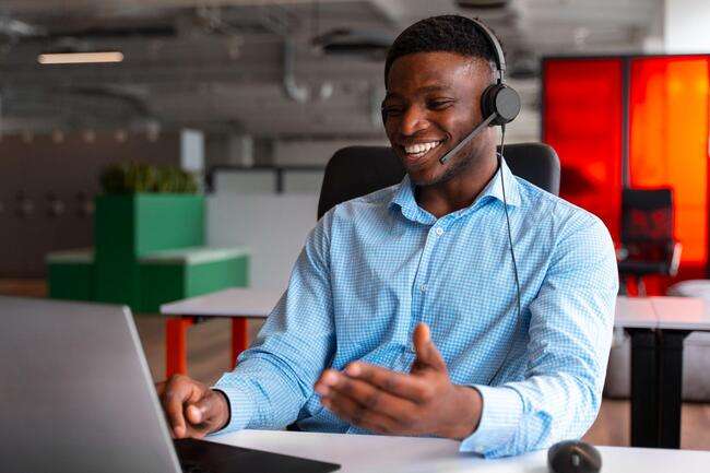 A man wearing a headset smiling and talking during a video call.