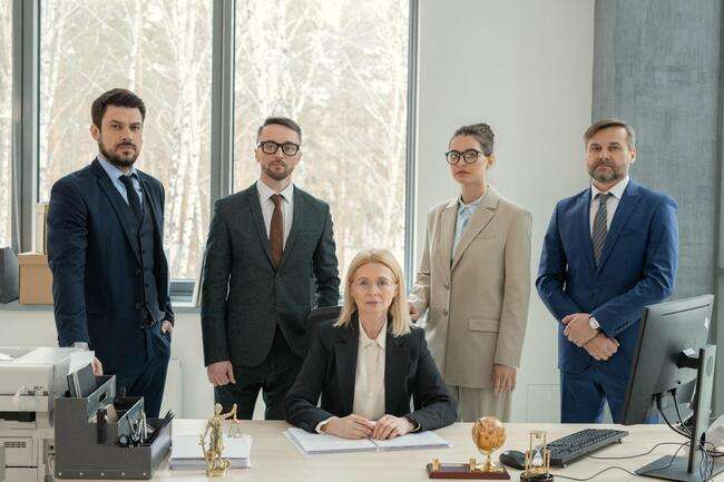 A diverse group of five business professionals standing confidently in an office, symbolizing a successful legal team.